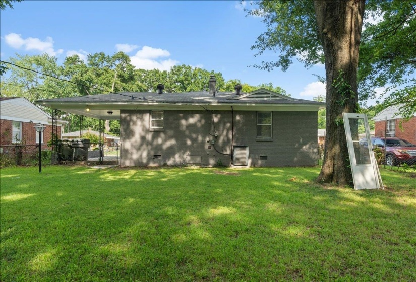 Spacious backyard featuring a covered patio, mature shade tree, and a brick exterior