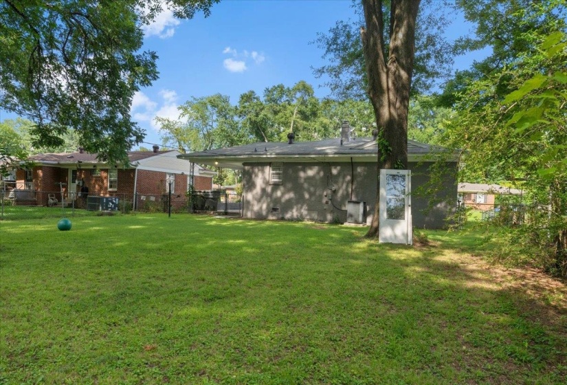 Expansive grassy yard with mature trees and a privacy fence