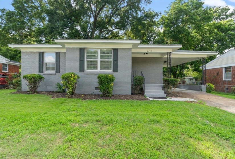 Gray brick exterior featuring a carport with decorative ironwork, a concrete driveway, and a front entry with steps and a handrail