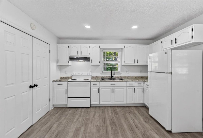 Bright kitchen featuring white cabinetry with dark hardware, a white range, a white refrigerator, light-toned countertops, and wood-finish flooring