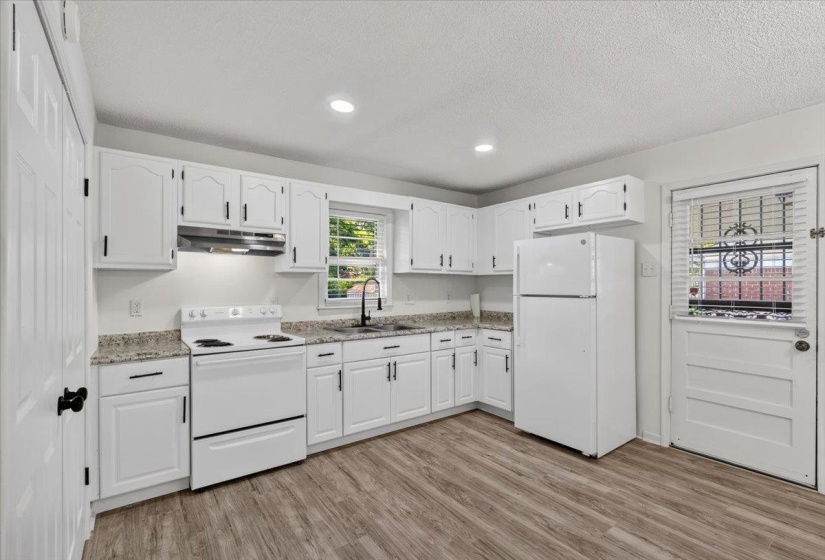 Modern kitchen featuring white cabinetry, granite-style countertops, stainless steel sink with a matte black faucet, recessed lighting, and wood-finish flooring