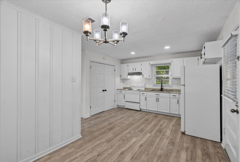 Eat-in kitchen featuring wood-finish flooring, white cabinetry, integrated appliances, and a modern chandelier