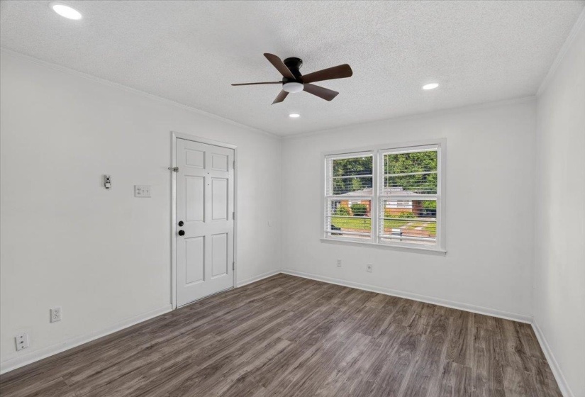 Bright room featuring wood-finish flooring, a white paneled door, a ceiling fan with integrated lighting, recessed lighting, and a double window with blinds