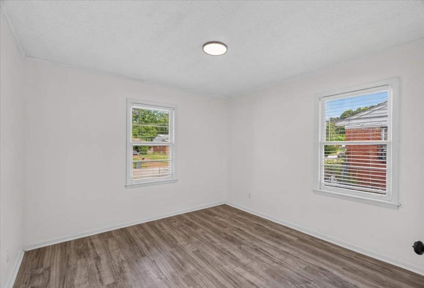 Room featuring wood-finish flooring, two windows with blinds, and white walls