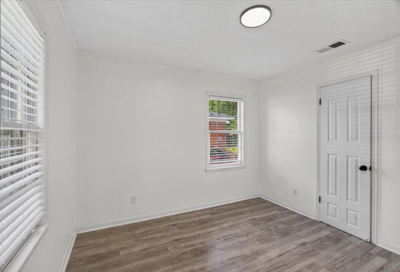 Room with wood-finish flooring, two windows with blinds, a white paneled door, and a flush-mount ceiling light