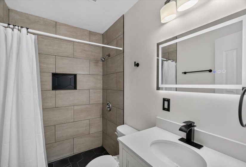 Contemporary bathroom featuring a tiled shower with recessed niche, a modern vanity with integrated sink, and an illuminated mirror