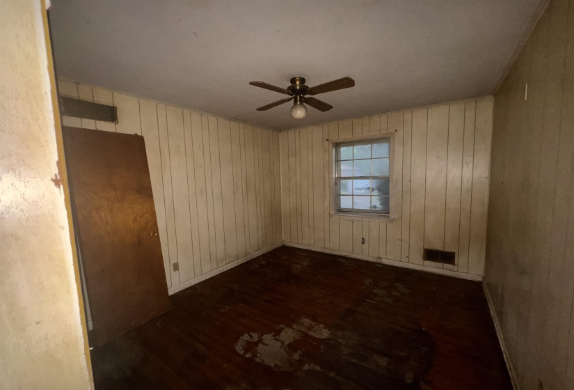 Room featuring wood-finish flooring, paneled walls, a single-pane window, and a ceiling fan with integrated lighting