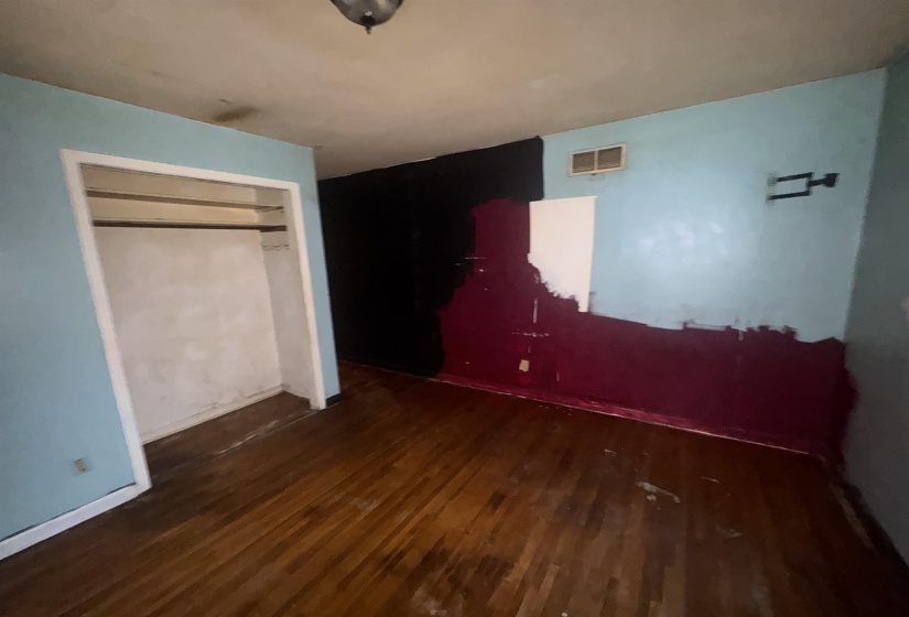 Room featuring wood-finish flooring, an open closet with a hanging rod, a ceiling-mounted light fixture, and an upper wall vent