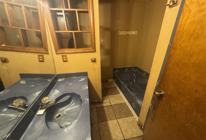 Bathroom featuring a built-in tub, dual sink vanity, tile flooring, and wood-framed mirror