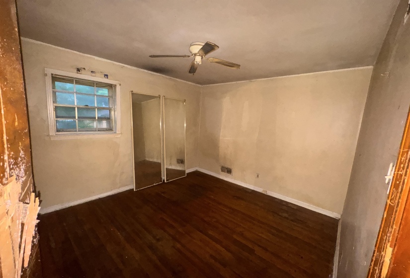 Interior space featuring wood-finish flooring, a ceiling fan with light fixture, a window with exterior visibility, and a mirrored closet door