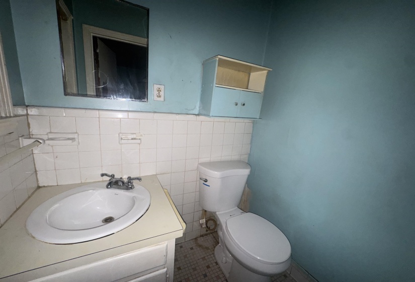 Bathroom featuring a drop-in sink with a double-handle faucet, a wall-mounted mirror, white ceramic wall tiling, and a built-in toilet