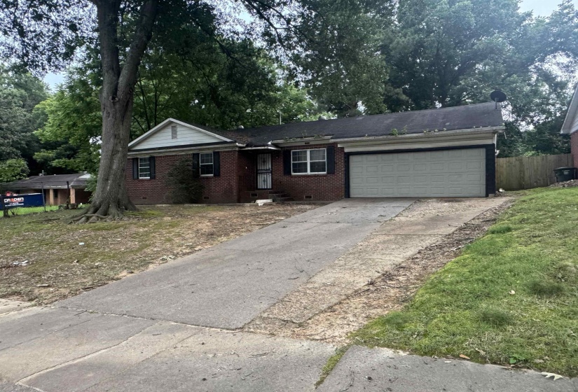 Brick-clad residence featuring an attached two-car garage, a paved driveway, and mature landscaping