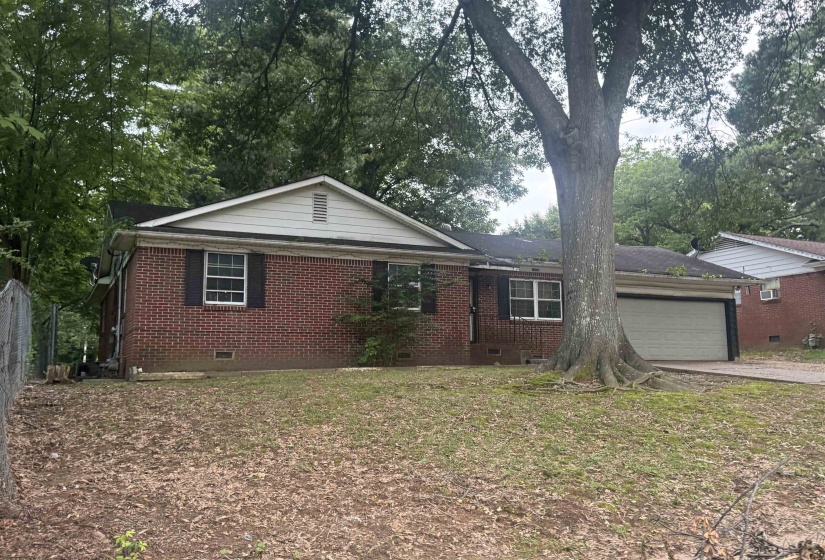 Brick facade residence featuring a front-facing attached garage and a mature tree in the front yard