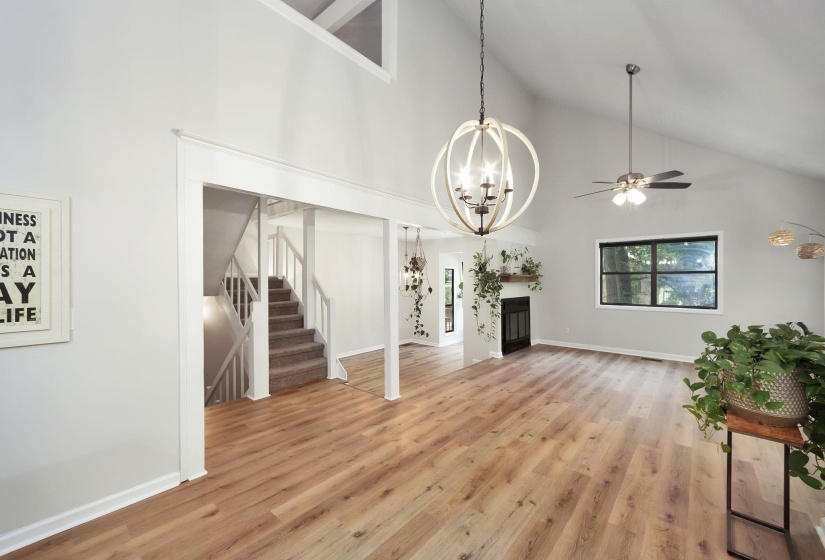 Vaulted ceiling living area featuring wood-finish flooring, a fireplace with a wood mantle, and a contemporary chandelier