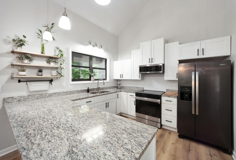 Kitchen featuring expansive stone countertops, white shaker cabinetry, stainless steel appliances, and wood-finish flooring