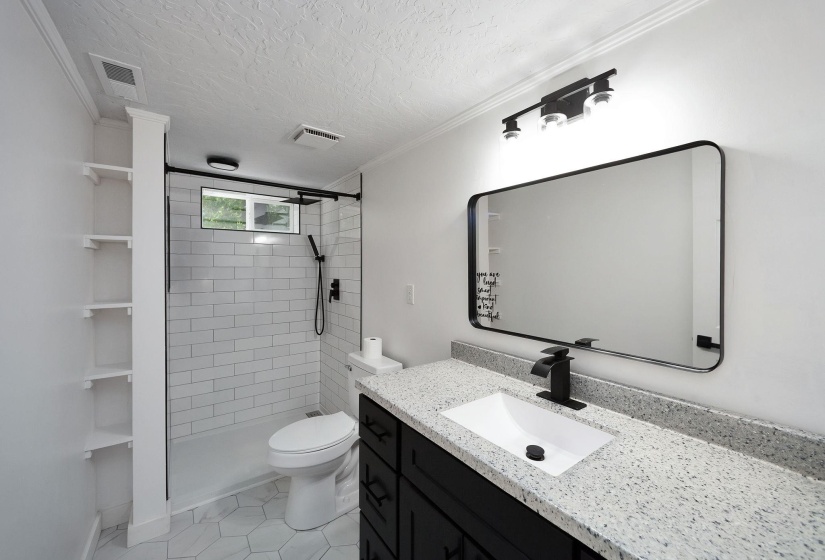 Bathroom featuring a quartz countertop vanity with a rectangular sink, matte black fixtures, a frameless shower with subway tile, white hexagon floor tile, and built-in shelving