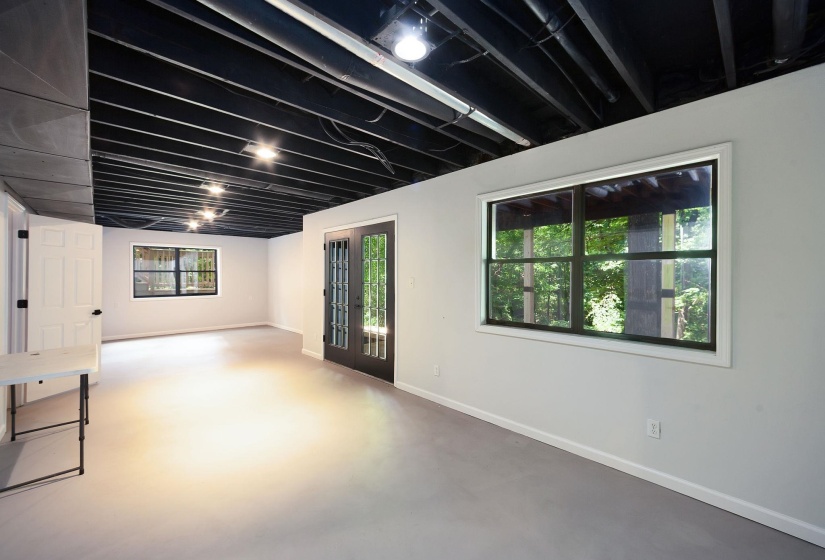 Spacious room featuring light gray walls, light gray flooring, and an exposed black painted ceiling with recessed lighting