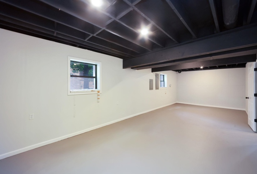 Spacious interior with a neutral painted floor, white walls, and a black painted exposed beam ceiling