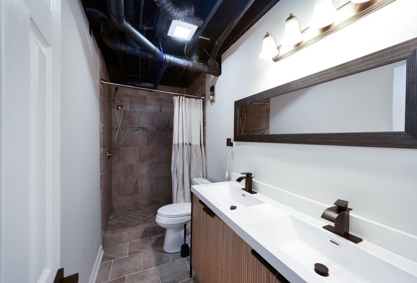 Bathroom featuring a dual vanity with white countertops and matte black faucets, a large framed mirror, and a tiled shower with a mosaic-tiled floor
