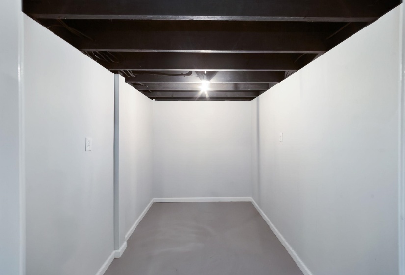 Unfinished basement space featuring light gray walls, white baseboards, and a painted gray concrete floor