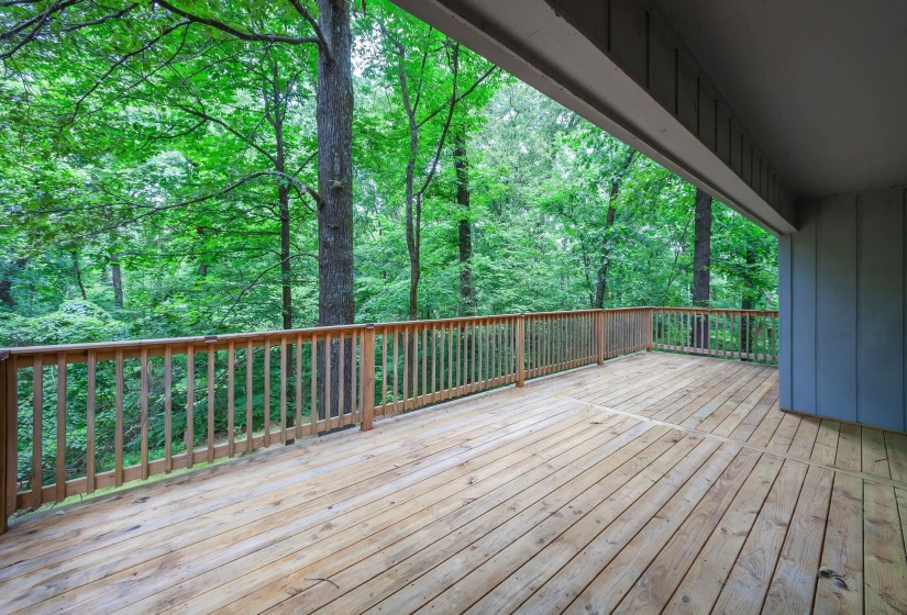 Expansive wood deck with natural wood railing, surrounded by mature trees