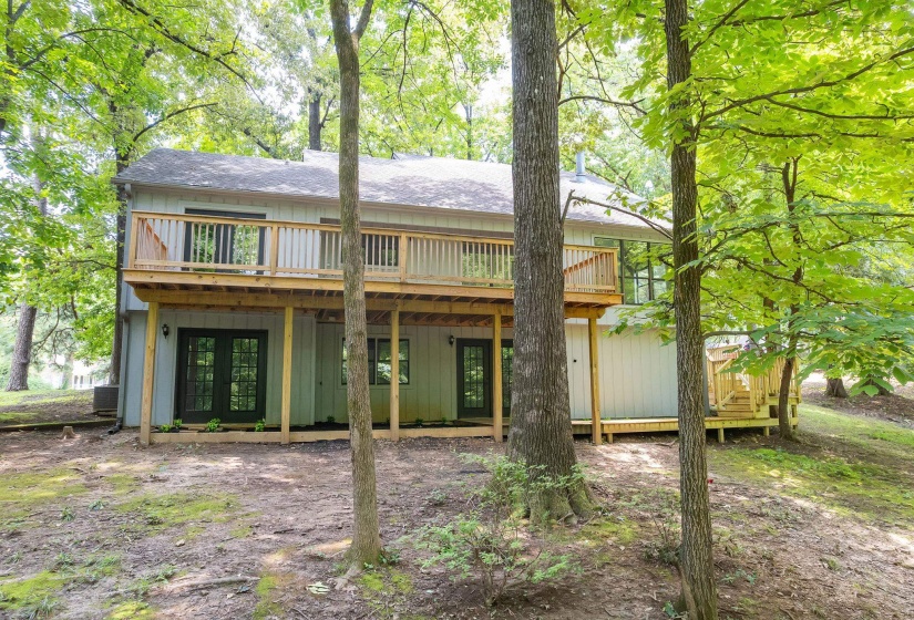 Rear exterior featuring a two-story deck with natural wood railings, multiple glass-paned doors on both levels, and a light-colored siding