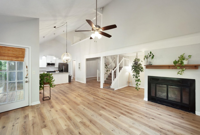 Spacious living area featuring vaulted ceilings, wood-finish flooring, and a fireplace with a wood mantle