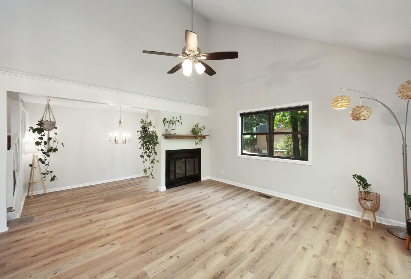 Vaulted ceiling living area featuring wood-finish flooring, a contemporary ceiling fan, and a fireplace with a wood mantel