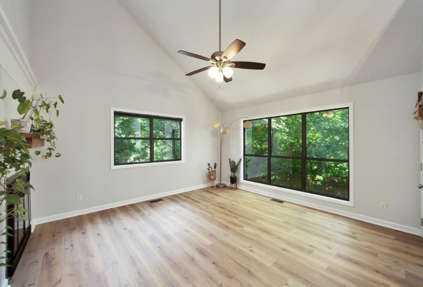 Vaulted ceilings accent this room featuring wood-finish flooring, a contemporary ceiling fan, and large black-framed windows