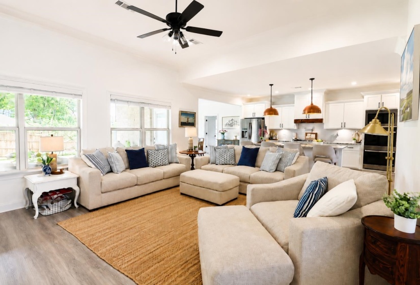 Open-concept living area featuring high vaulted ceilings with a ceiling fan, light wood-finish flooring, and multiple windows