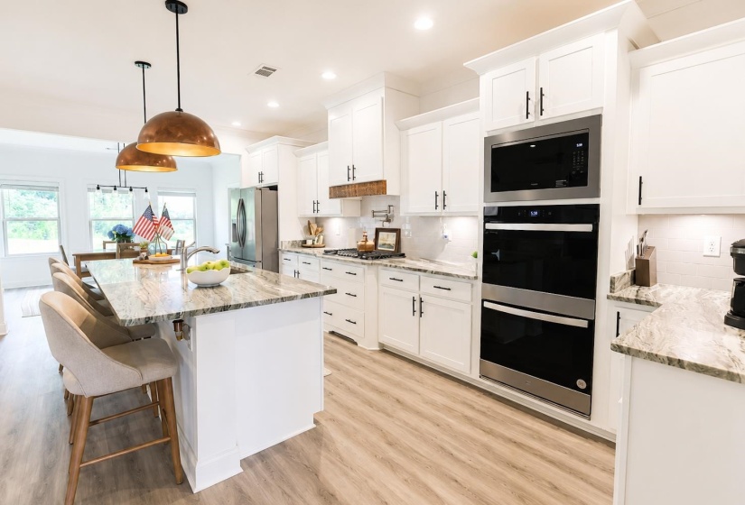 Kitchen featuring a central island with a sink, light-toned granite countertop, and pendant lighting