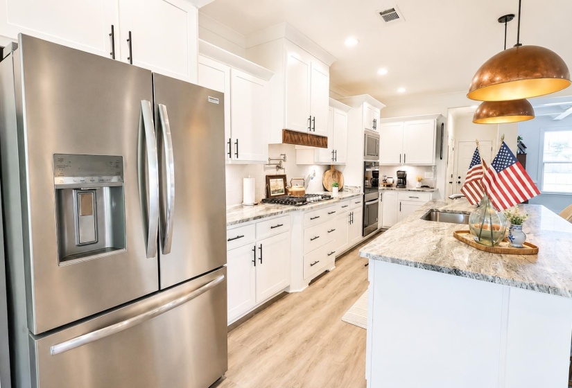 Modern kitchen featuring white cabinetry, light wood-finish flooring, a stainless steel French door refrigerator, a central island with a sink, and pendant lighting
