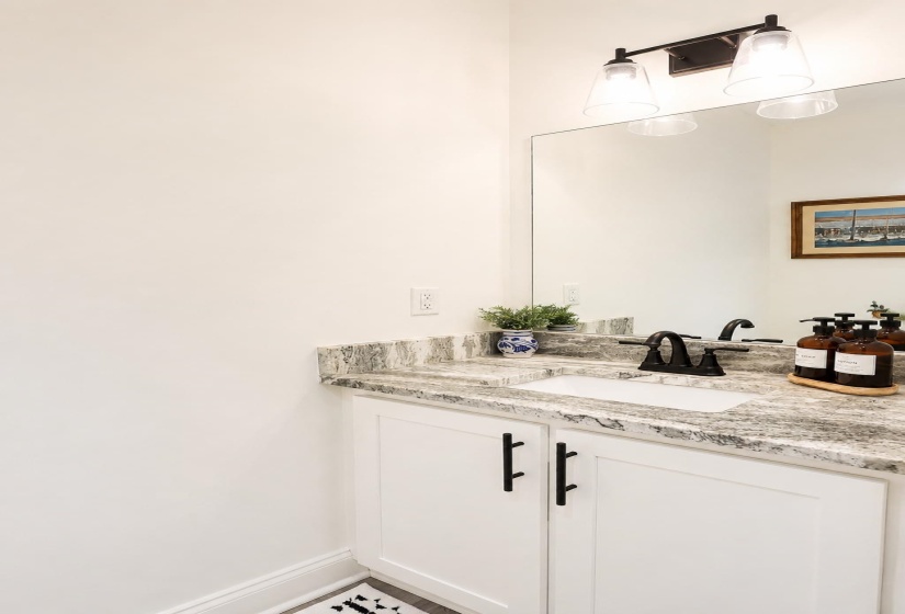 Bathroom vanity featuring white shaker-style cabinetry with matte black hardware, a granite countertop, and an undermount sink with a matte black faucet