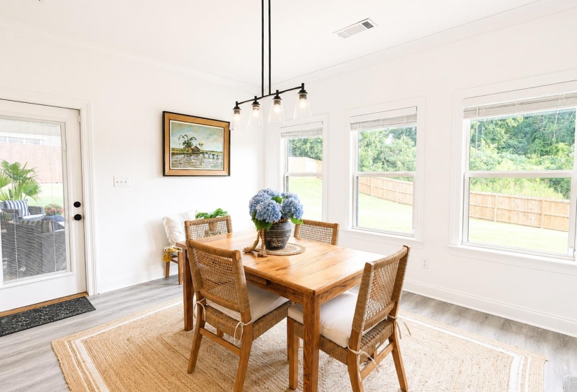 Naturally lit dining area featuring light wood-finish flooring, a contemporary linear chandelier, and access to an exterior patio through a glass-paned door