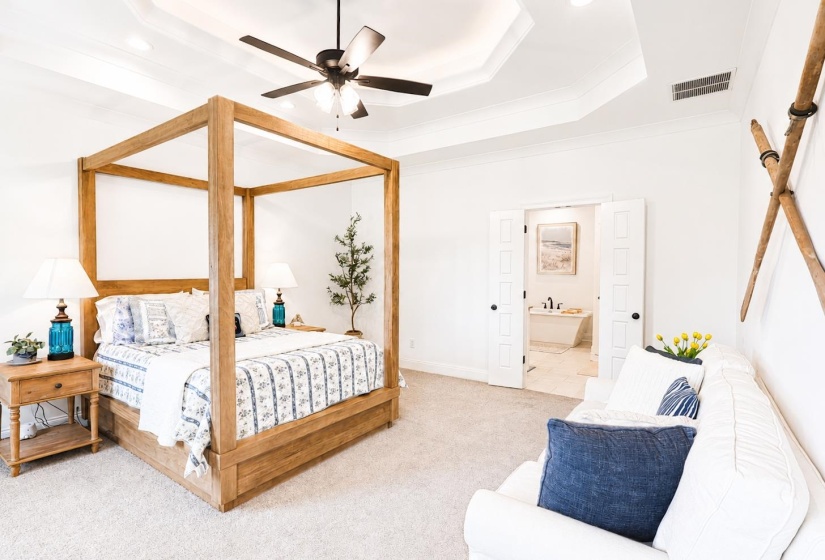 Recessed lighting and a tray ceiling illuminate this bedroom featuring plush carpet flooring and a ceiling fan