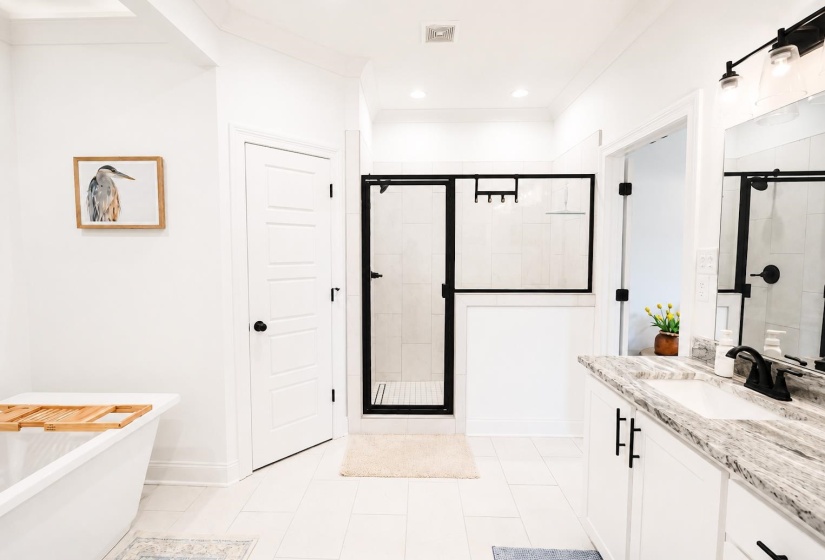 Modern bathroom featuring a freestanding tub, glass-enclosed shower with black framing, white tile flooring, double vanity with stone countertop, and matte black fixtures