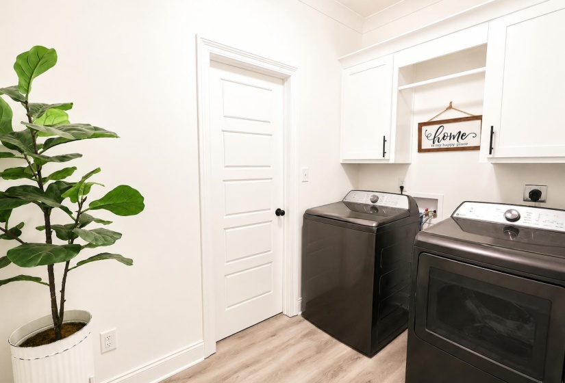 Dedicated laundry area featuring white shaker-style cabinetry with matte black hardware, a built-in hanging rod, and light wood-finish flooring