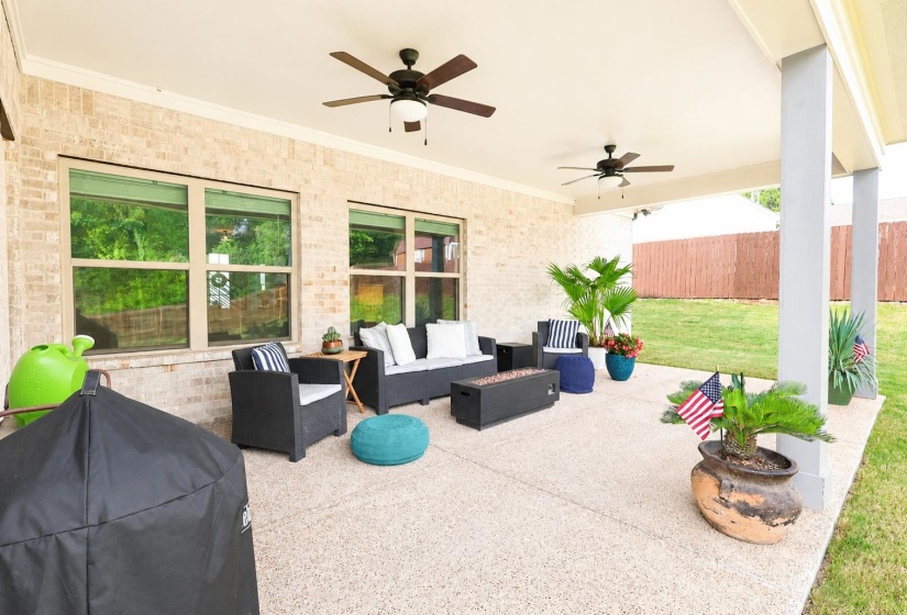 Spacious covered patio with textured concrete flooring, brick exterior, two ceiling fans, and recessed lighting