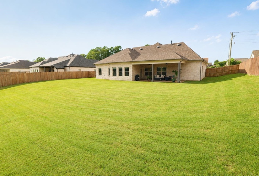 Expansive rear lawn featuring a privacy fence, covered patio, brick exterior, and multiple rear-facing windows