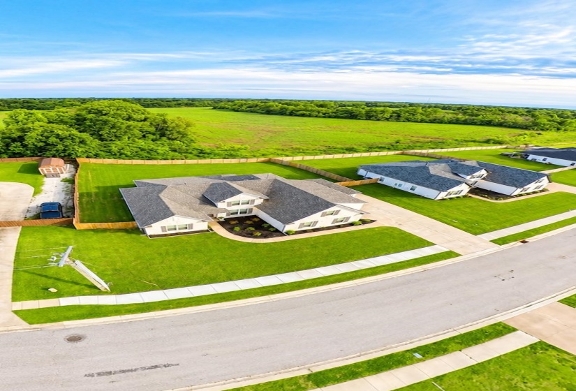 Aerial view of a contemporary home featuring a light-colored exterior, dark shingle roof, and a meticulously landscaped front yard