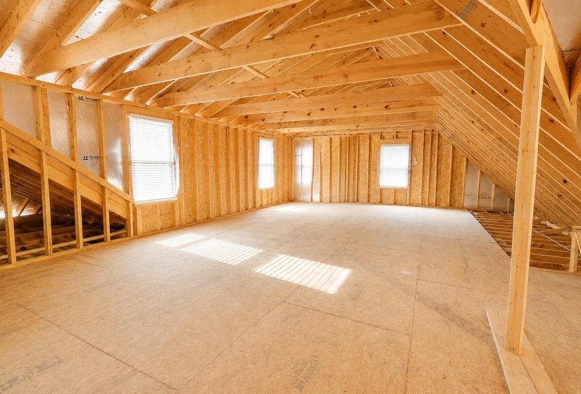 Unfinished attic space featuring exposed wood framing, multiple windows, and a partially finished subfloor