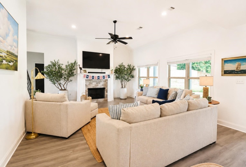 Spacious living area featuring vaulted ceilings, recessed lighting, a ceiling fan, a fireplace with a stone surround, and wood-finish flooring