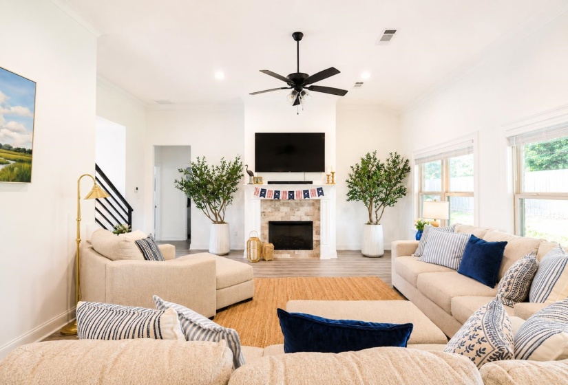 Spacious living area featuring a vaulted ceiling with a ceiling fan, a stone-faced fireplace, and wood-finish flooring