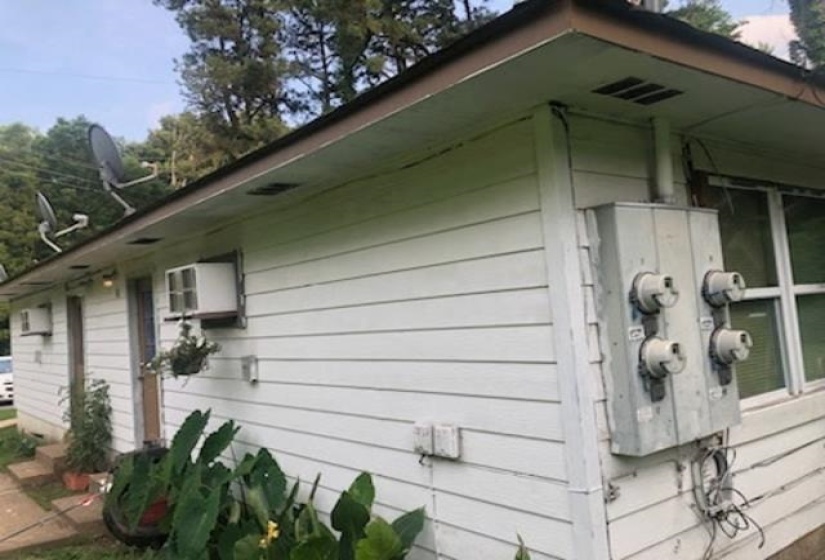 White horizontal siding exterior with multiple window-mounted air conditioning units, exposed utility meters, and a dark shingle roof