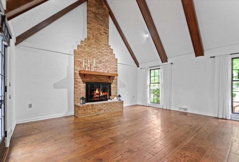 Unfurnished living room featuring beamed ceiling, wood-type flooring, a fireplace, visible vents, and high vaulted ceiling
