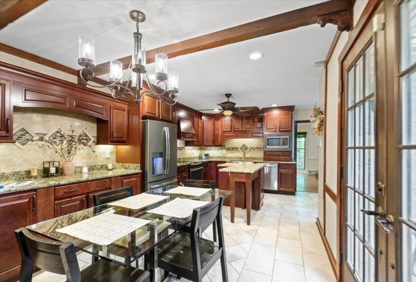 Kitchen featuring decorative backsplash, appliances with stainless steel finishes, recessed lighting, custom exhaust hood, and ceiling fan with notable chandelier