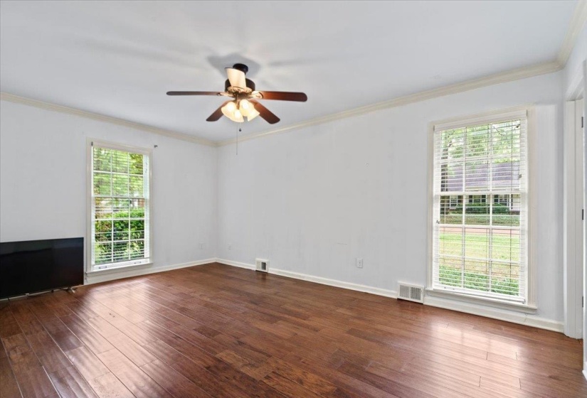 Unfurnished room featuring dark wood-style floors, visible vents, a ceiling fan, and a healthy amount of sunlight
