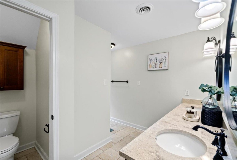 Bathroom with a sink, double vanity, visible vents, baseboards, and toilet