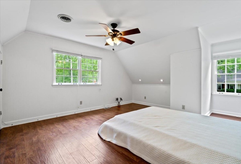 Bedroom with wood-type flooring, visible vents, vaulted ceiling, and multiple windows