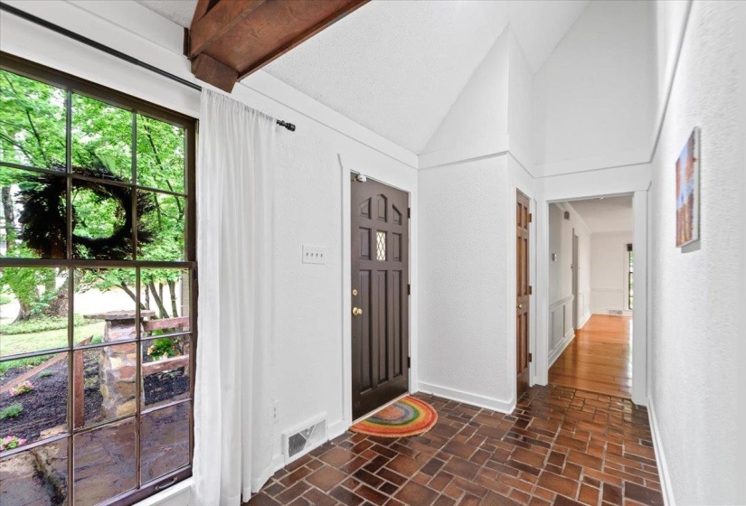 Foyer with visible vents, brick floor, vaulted ceiling, and baseboards